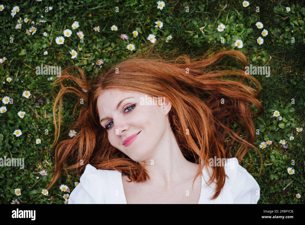 Donna sorridente di testa rossa sdraiata sull'erba Foto Stock