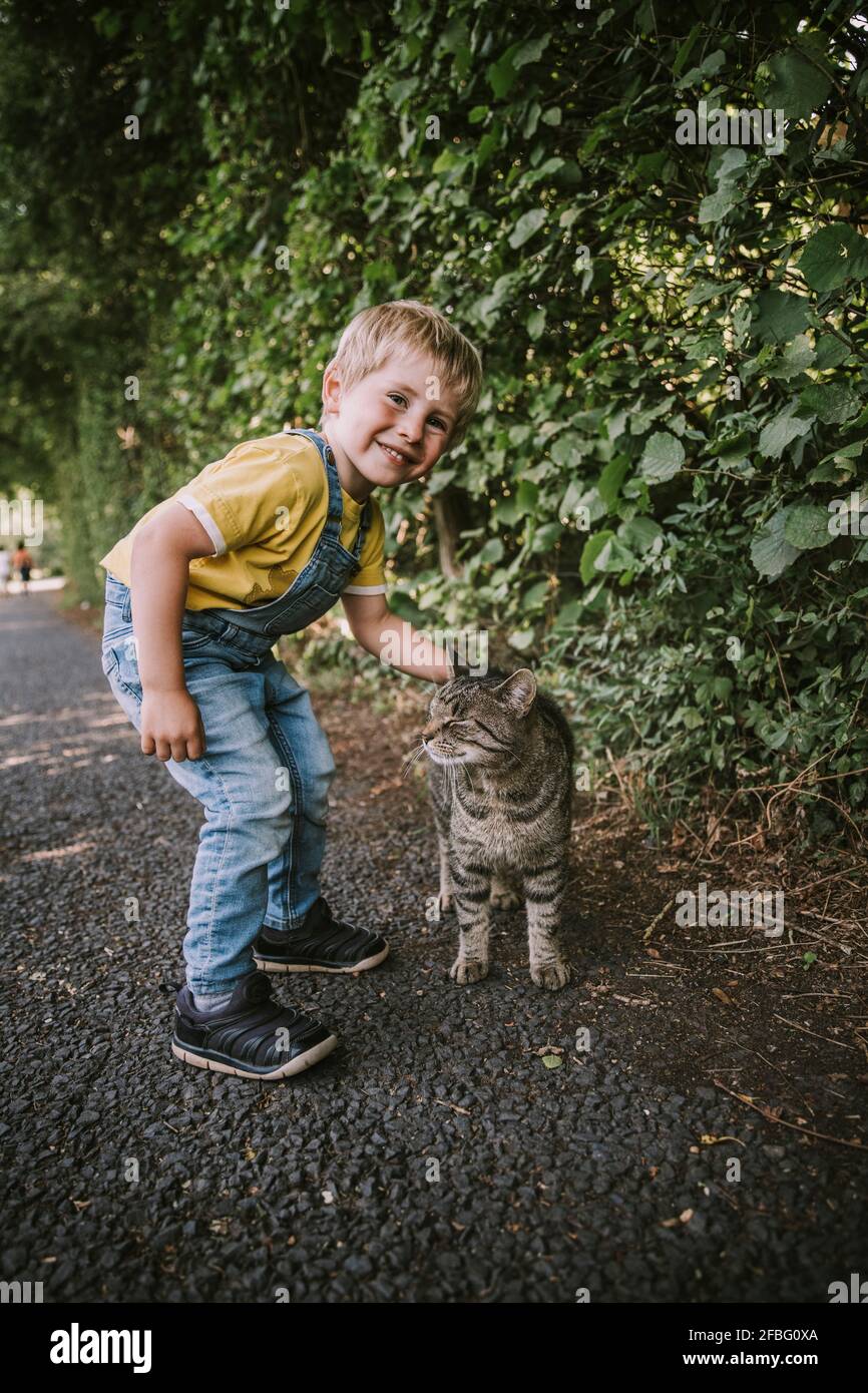 Carino ragazzo stroking gatto randagio sulla strada Foto Stock