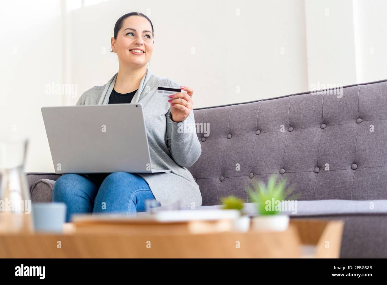 Donna sorridente che guarda via mentre acquista in linea usando la carta di credito su un computer portatile Foto Stock