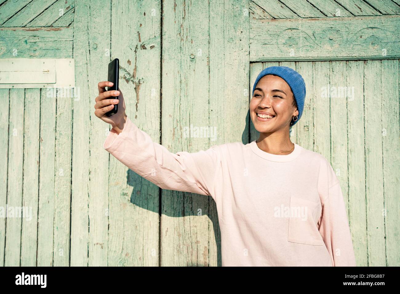 Donna felice in cappello a maglia prendendo selfie attraverso il telefono cellulare durante il giorno di sole Foto Stock