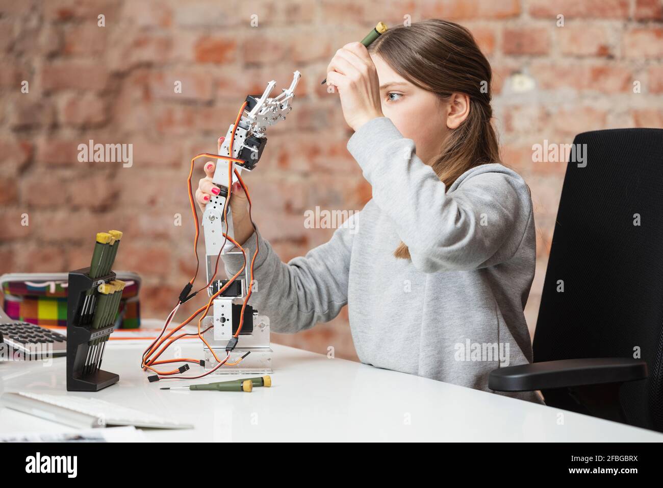 Ragazza che tiene il braccio robotico e l'attrezzatura al tavolo Foto Stock