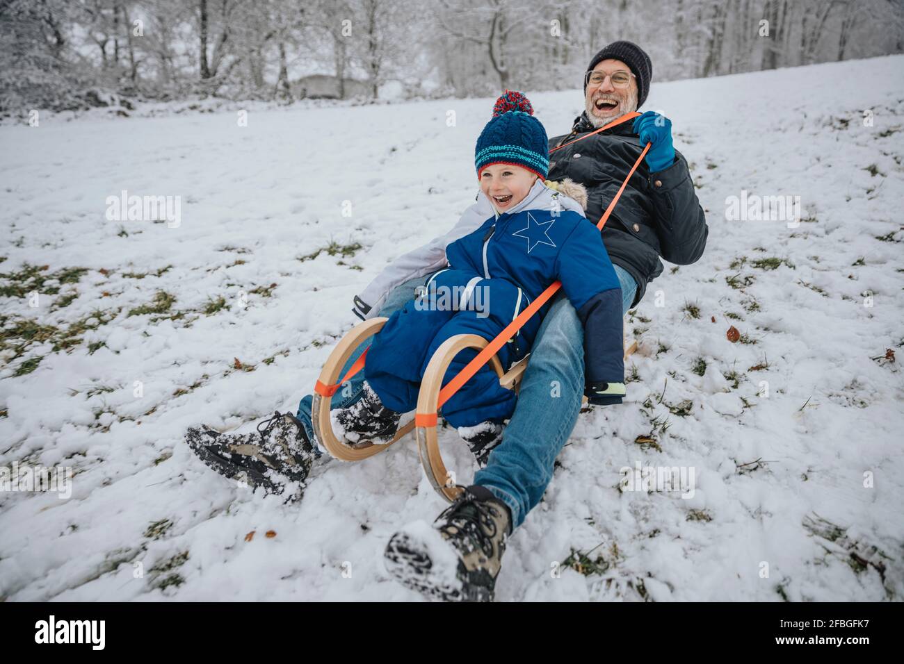 Il padre e il figlio allegri dormono lungo la collina innevata durante l'inverno Foto Stock