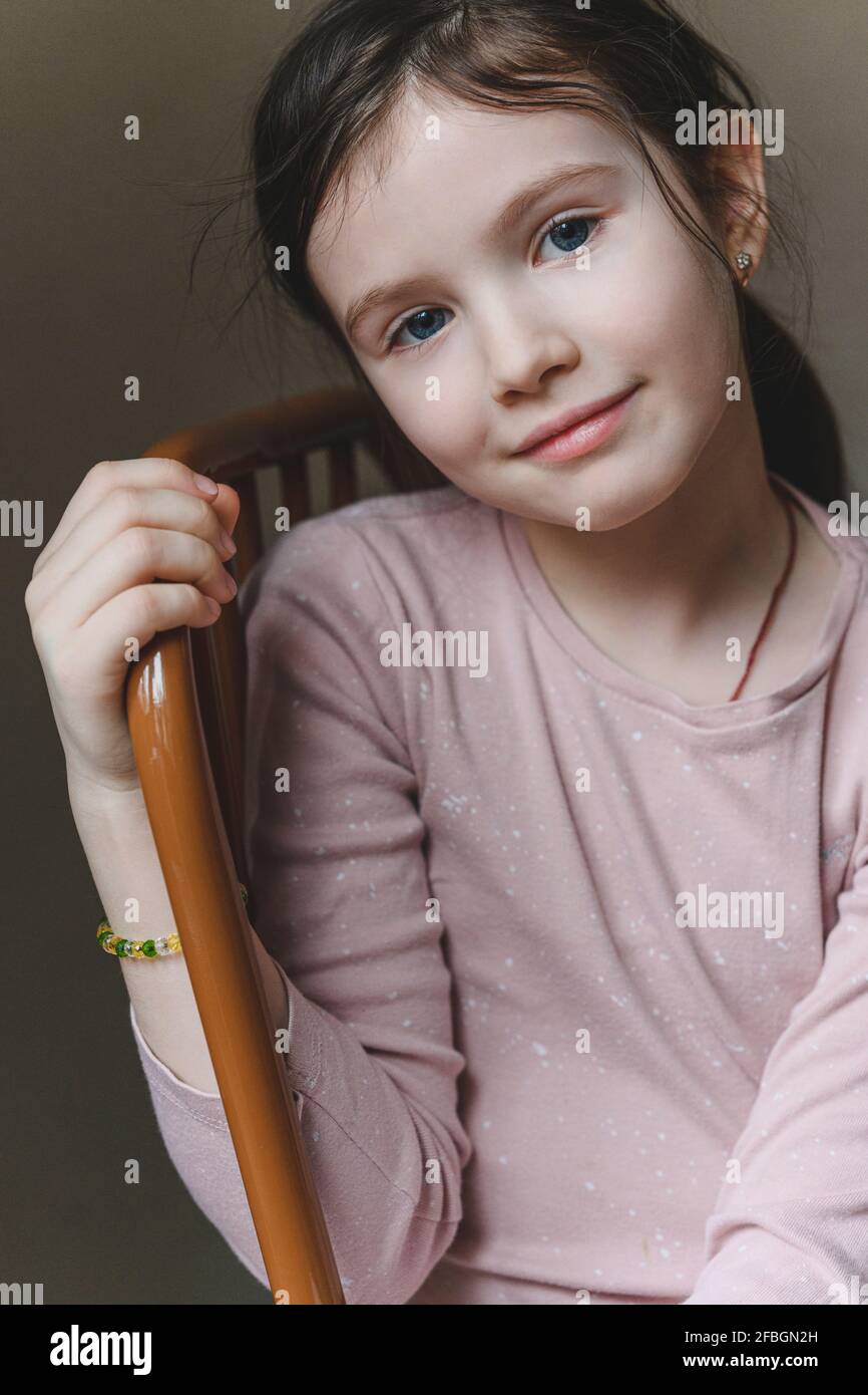 Ragazza sorridente con gli occhi blu seduti sulla sedia a casa Foto Stock