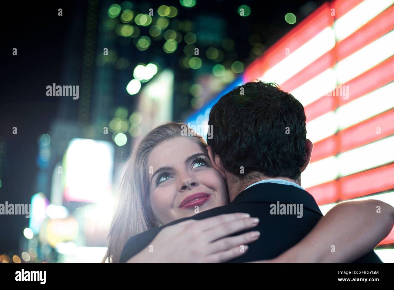 Bella donna che abbraccia il ragazzo con luci illuminate in città Foto Stock