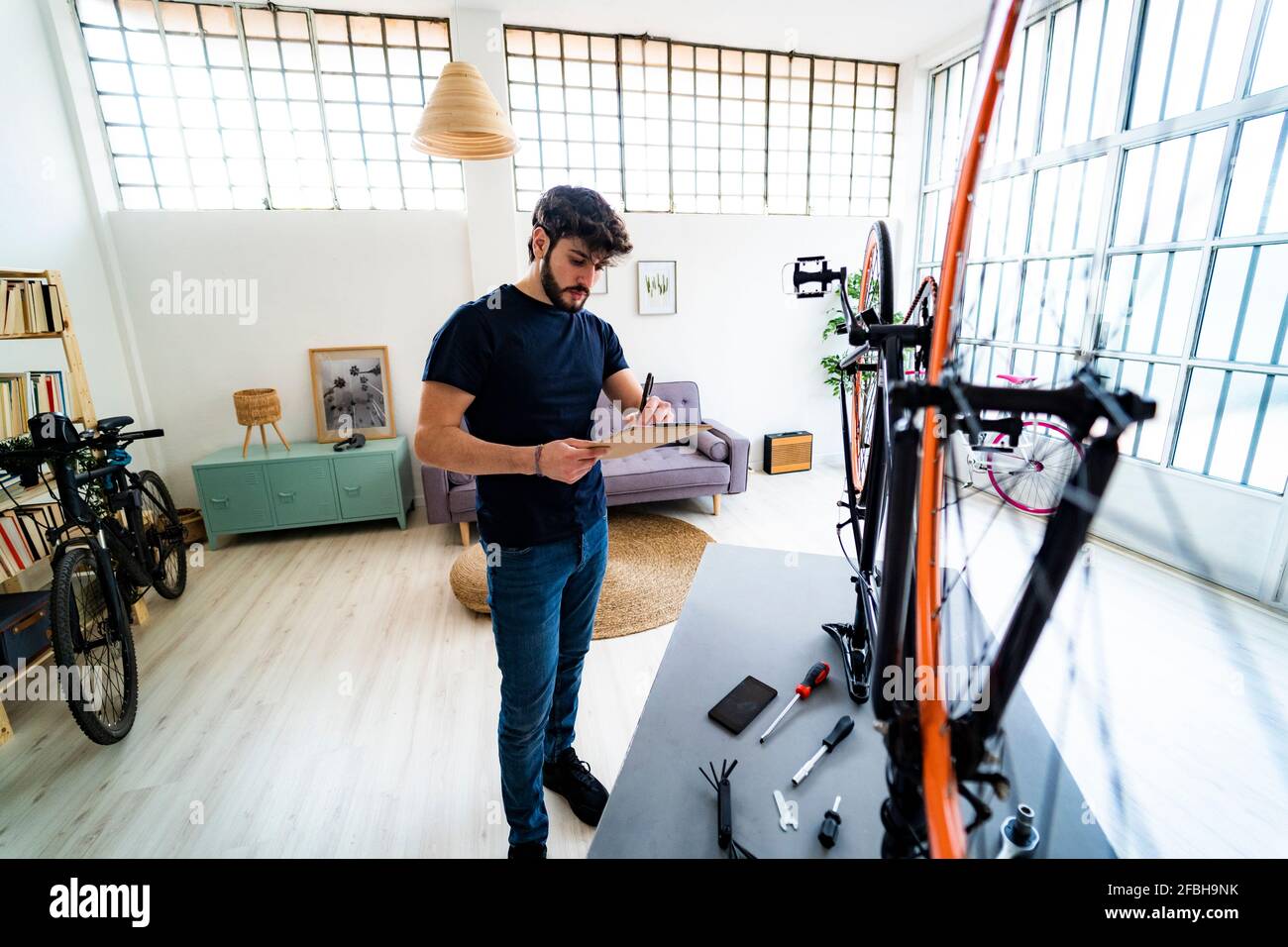 Giovane uomo che scrive note mentre ripara la bicicletta a casa Foto Stock