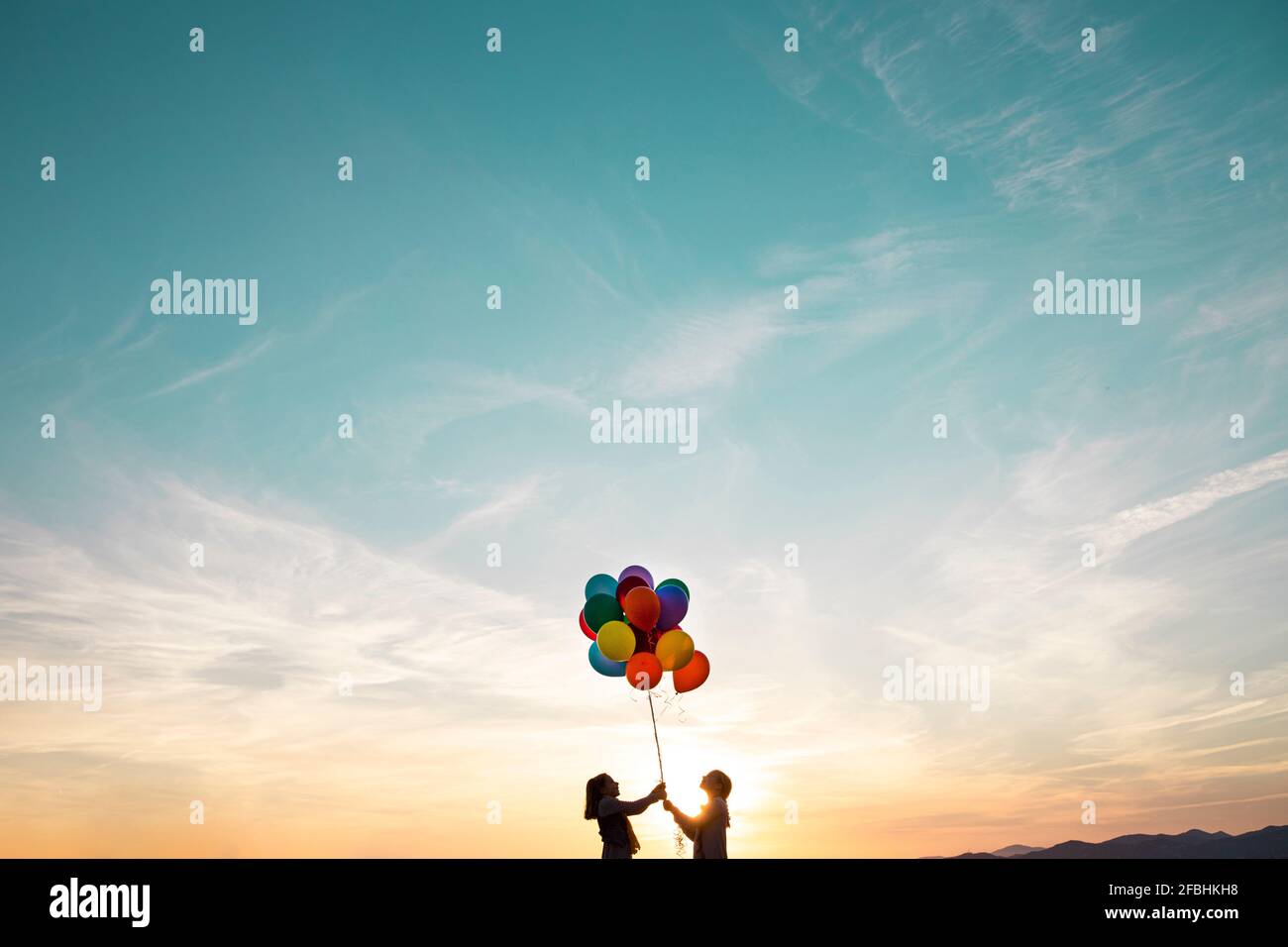 Ragazze in silhouette che giocano con palloncini multicolore durante il tramonto Foto Stock