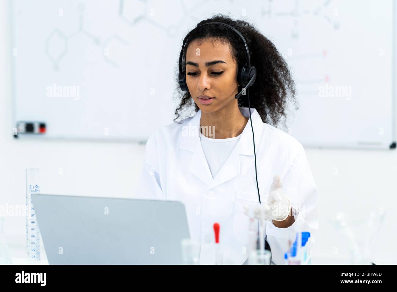 Giovane ricercatore che indossa le cuffie durante la videochiamata con il laptop in laboratorio Foto Stock