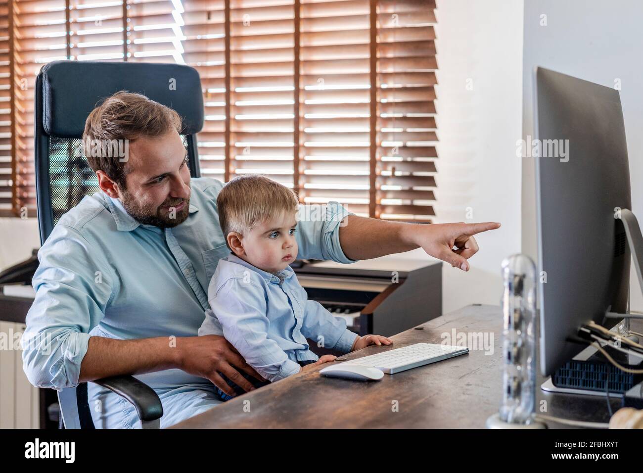 Sorridente padre che punta al computer mentre il figlio è seduto sul giro a casa Foto Stock