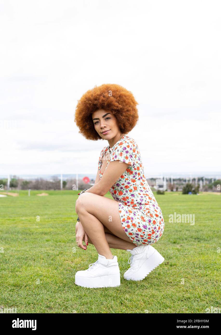 Donna afro rossa accovacciata sull'erba Foto Stock