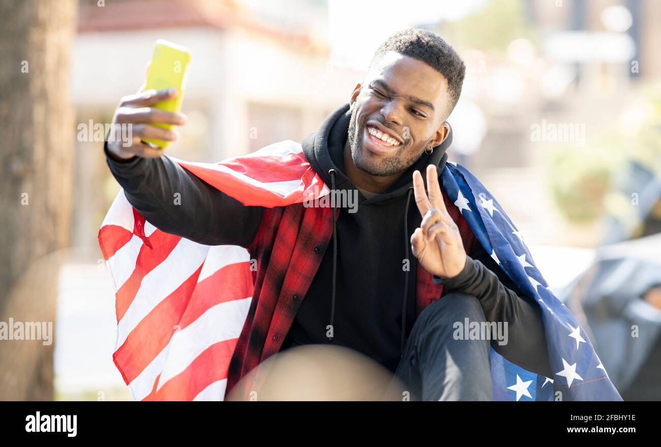 Giovane uomo che prende selfie con bandiera americana mentre mostra la pace cartello e verricello Foto Stock
