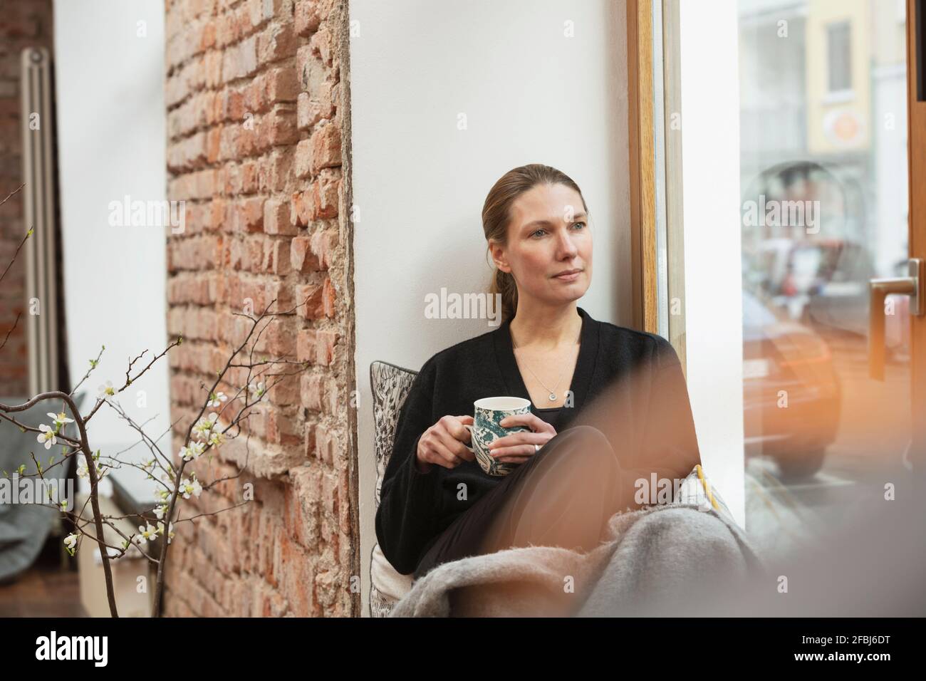 Donna professionale premurosa con tazza da tè seduto vicino alla finestra casa Foto Stock
