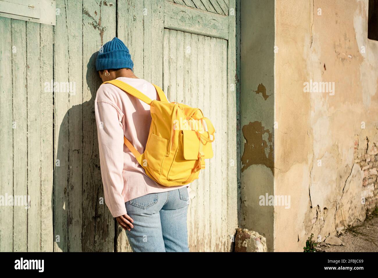 Lonely Woman con zaino giallo appoggiato su una vecchia porta di legno Foto Stock