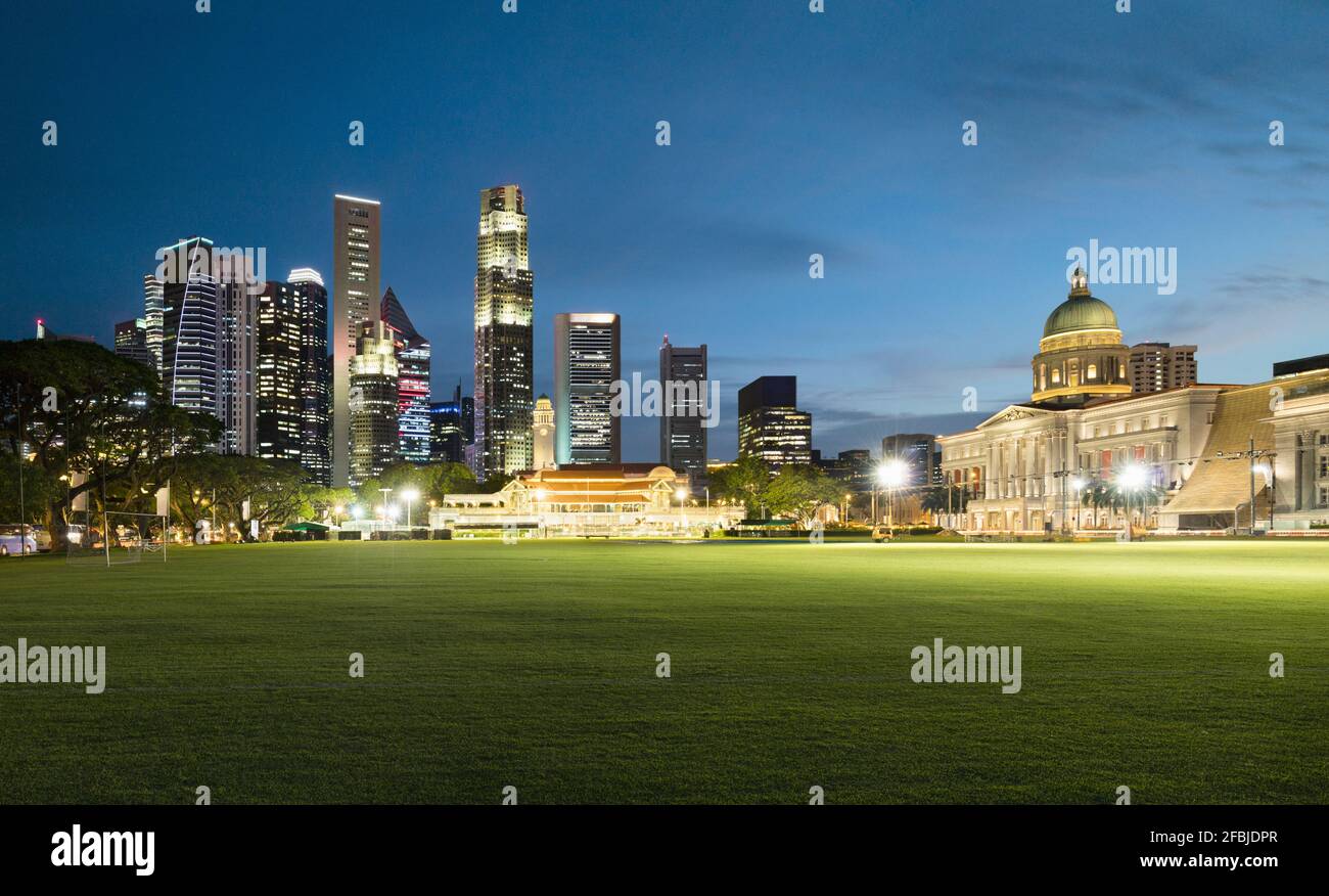 Singapore, Padang Field al crepuscolo con skyline illuminato della città sullo sfondo Foto Stock