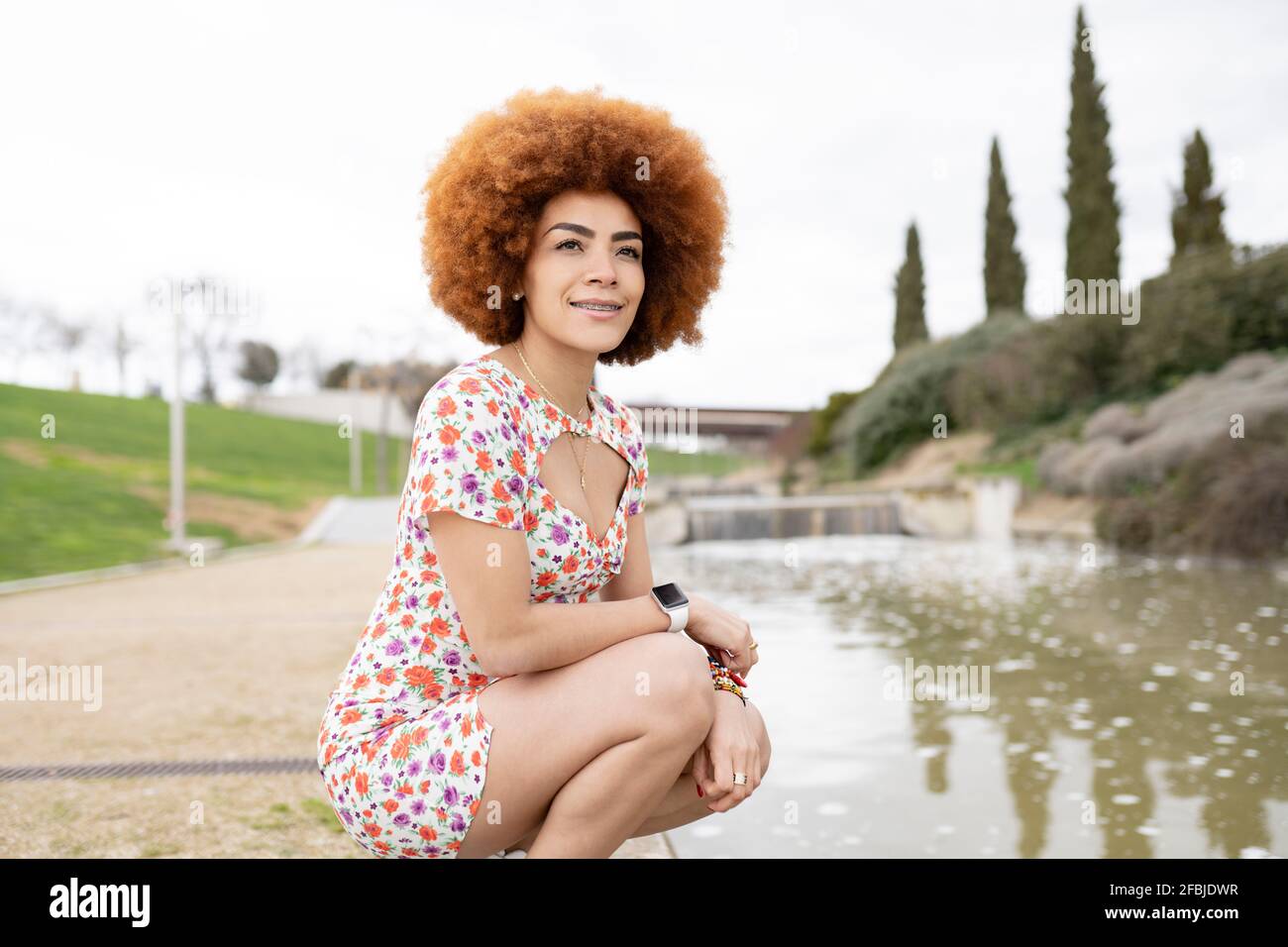 Redhead giovane donna accovacciata dall'acqua al parco Foto Stock
