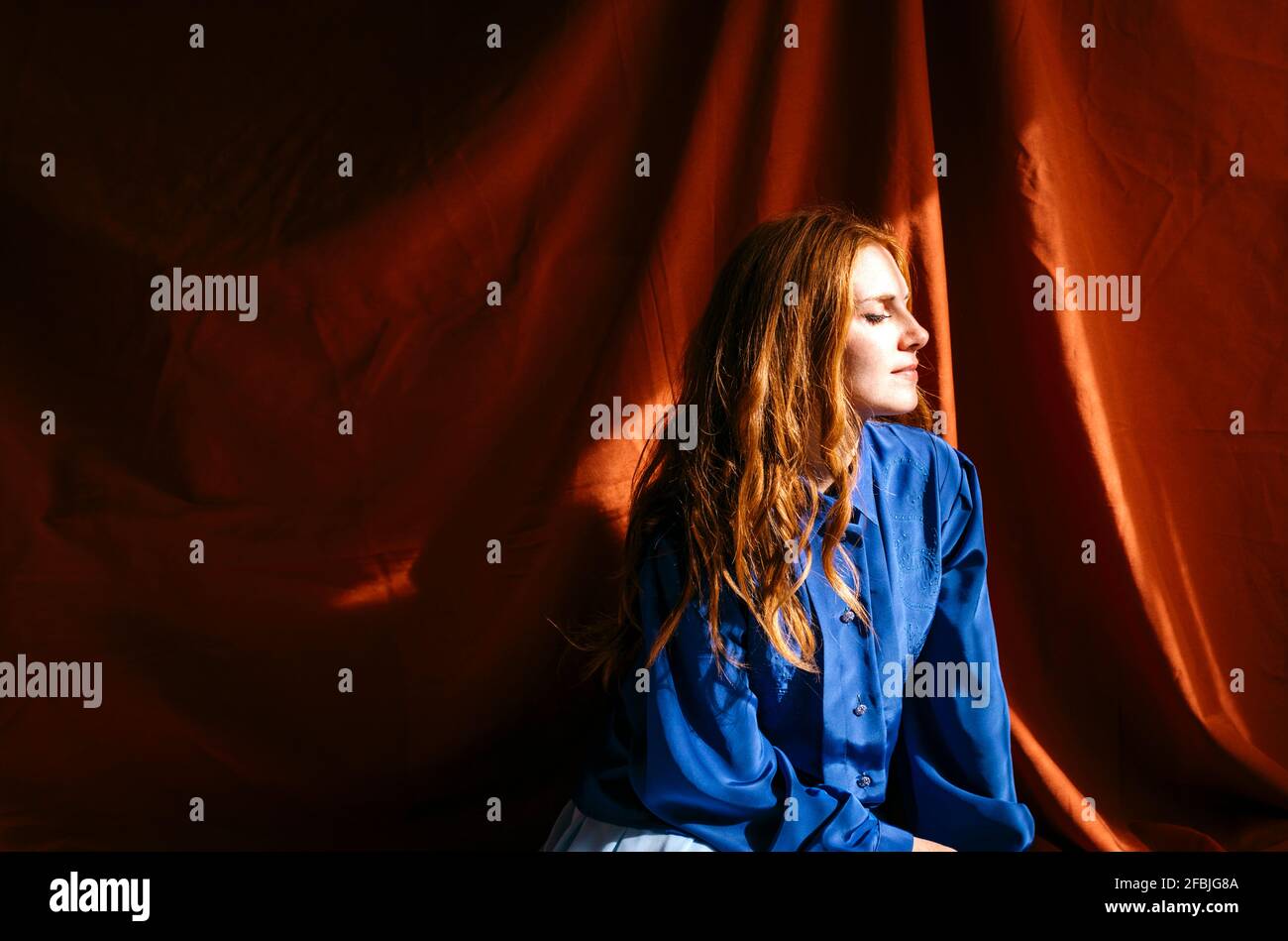 Giovane donna con gli occhi chiusi seduto di fronte a un panno rosso alla luce del sole Foto Stock