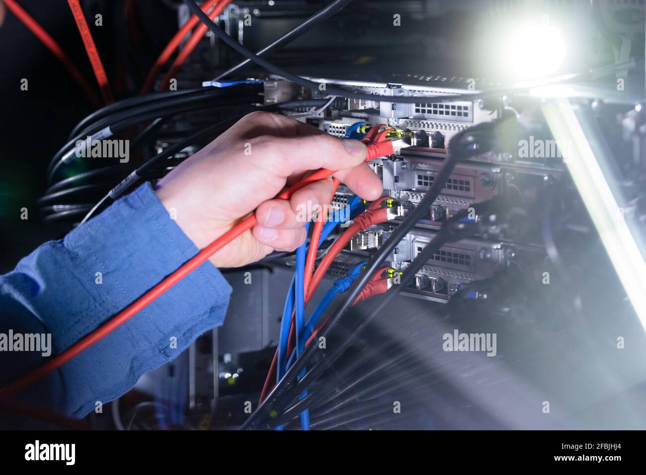 Tecnico IT maschio che collega il cavo patch nel rack server Foto Stock