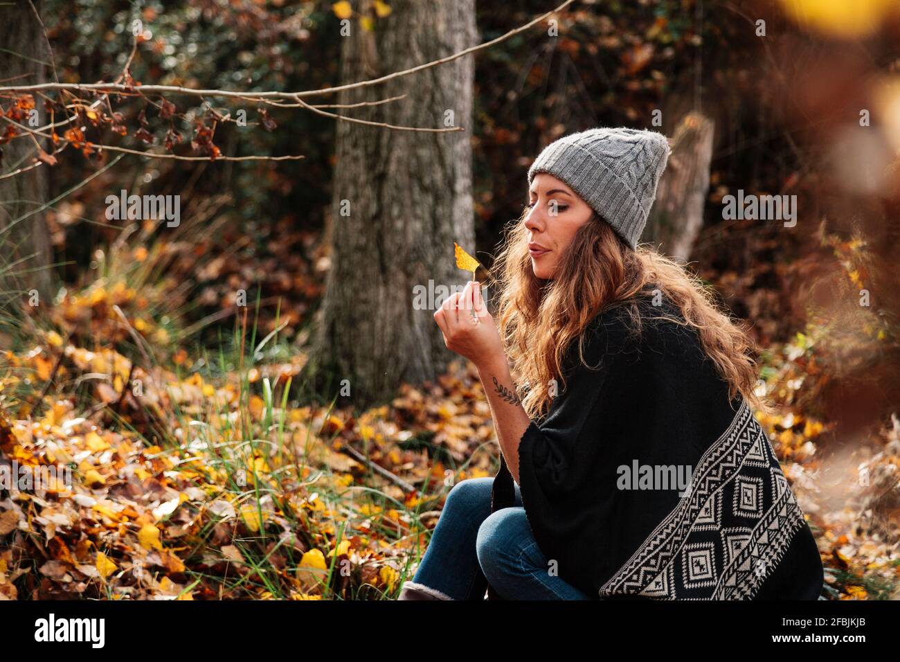 Bella donna con capelli lunghi che soffia foglia d'autunno in foresta durante le vacanze Foto Stock