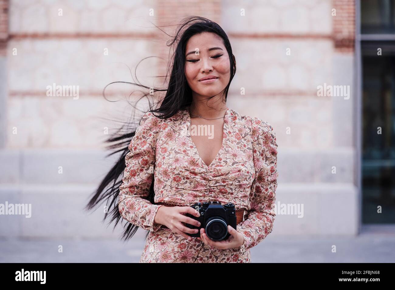 Donna sorridente con gli occhi chiusi tenendo la macchina fotografica a parete Foto Stock