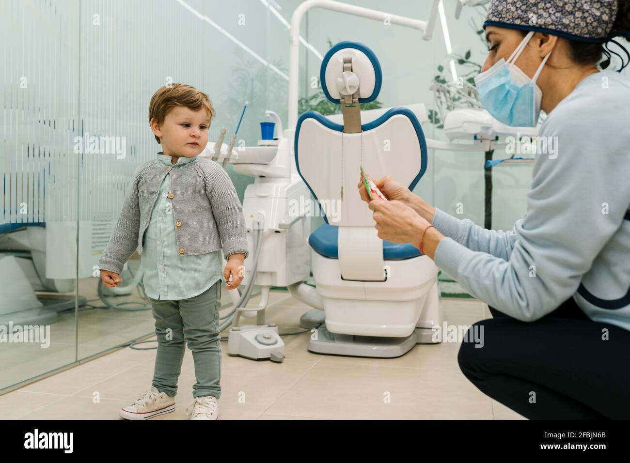 Bambino che guarda la dentista pediatrica femminile con il viso protettivo maschera in clinica Foto Stock