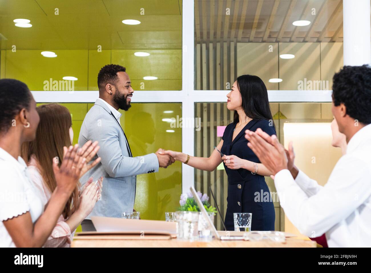 I colleghi si battono per gli imprenditori che fanno stretta di mano durante una riunione in ufficio Foto Stock