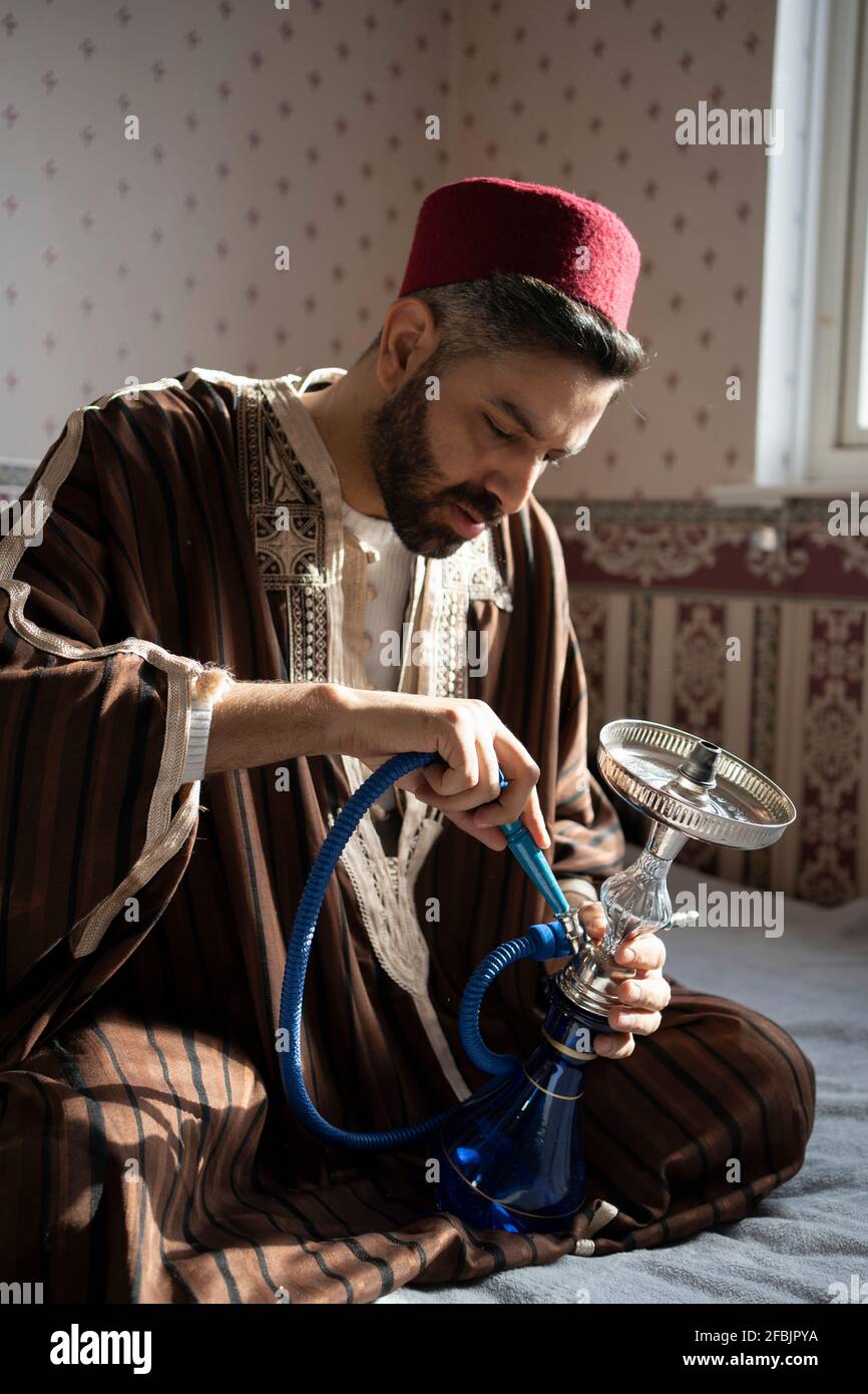 Uomo in abbigliamento tradizionale che tiene Hookah a casa Foto Stock