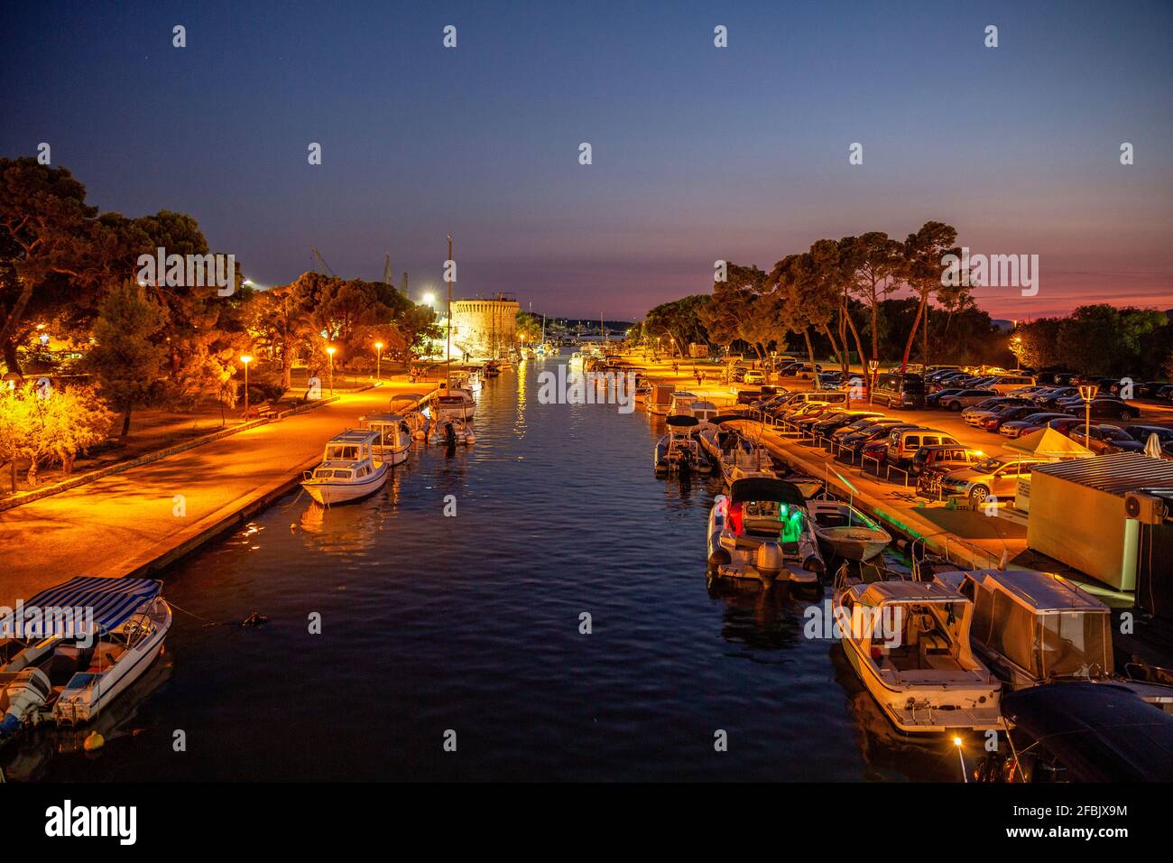 Croazia, Split-Dalmazia County, Trogir, barche a motore ormeggiate lungo il canale illuminato della città di notte Foto Stock