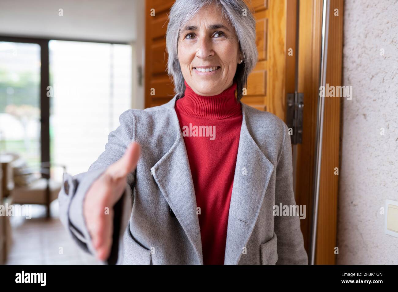 Donna matura sorridente che offre la stretta di mano alla porta Foto Stock