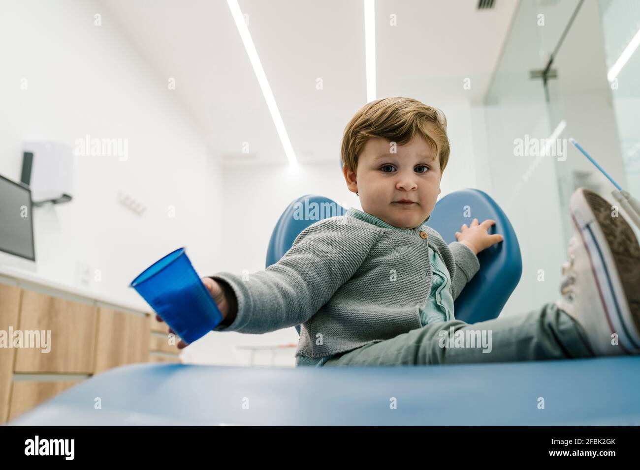Il bambino gioca con la tazza mentre si siede sulla sedia a. ufficio del  dentista Foto stock - Alamy