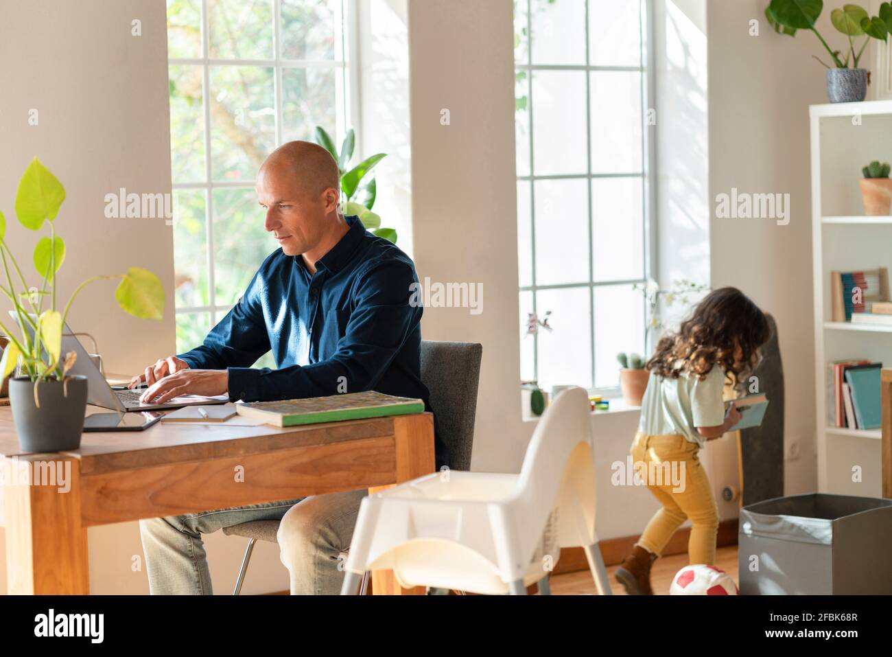 Padre che lavora da casa su un computer portatile mentre il suo bambino gioca in background Foto Stock