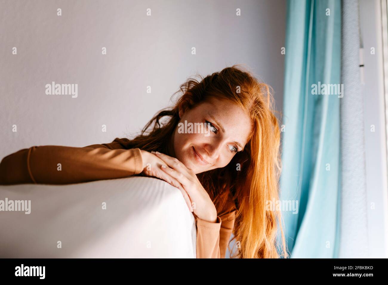 Giovane donna sorridente con mano sul mento guardando giù a casa Foto Stock