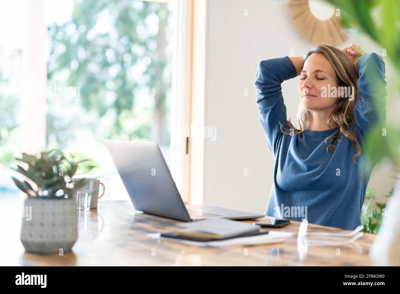 Seduta femminile rilassata con gli occhi chiusi mentre si prende la pausa dal lavoro a casa Foto Stock