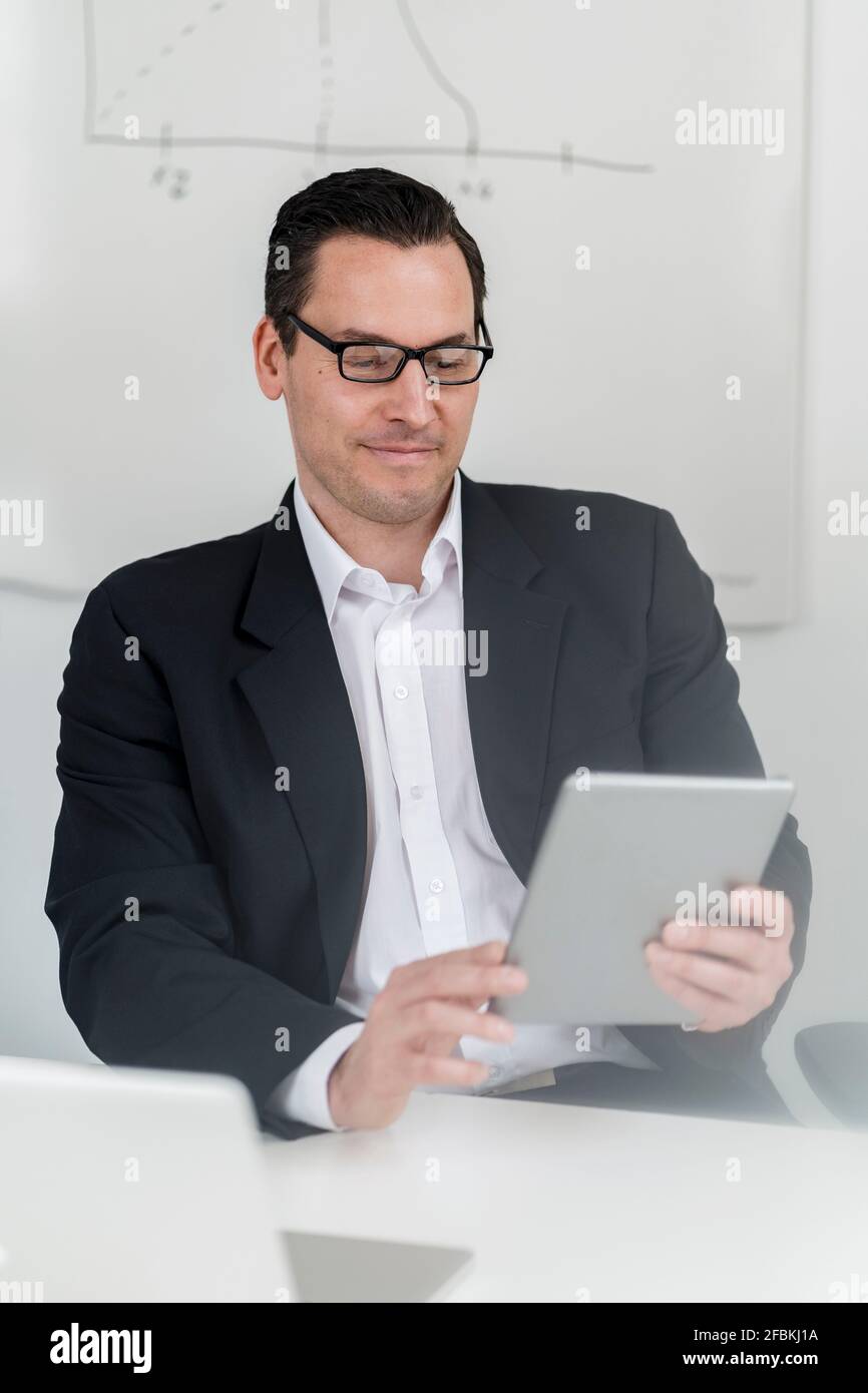 Imprenditore maschile seduto e che utilizza un tablet digitale sul posto di lavoro Foto Stock
