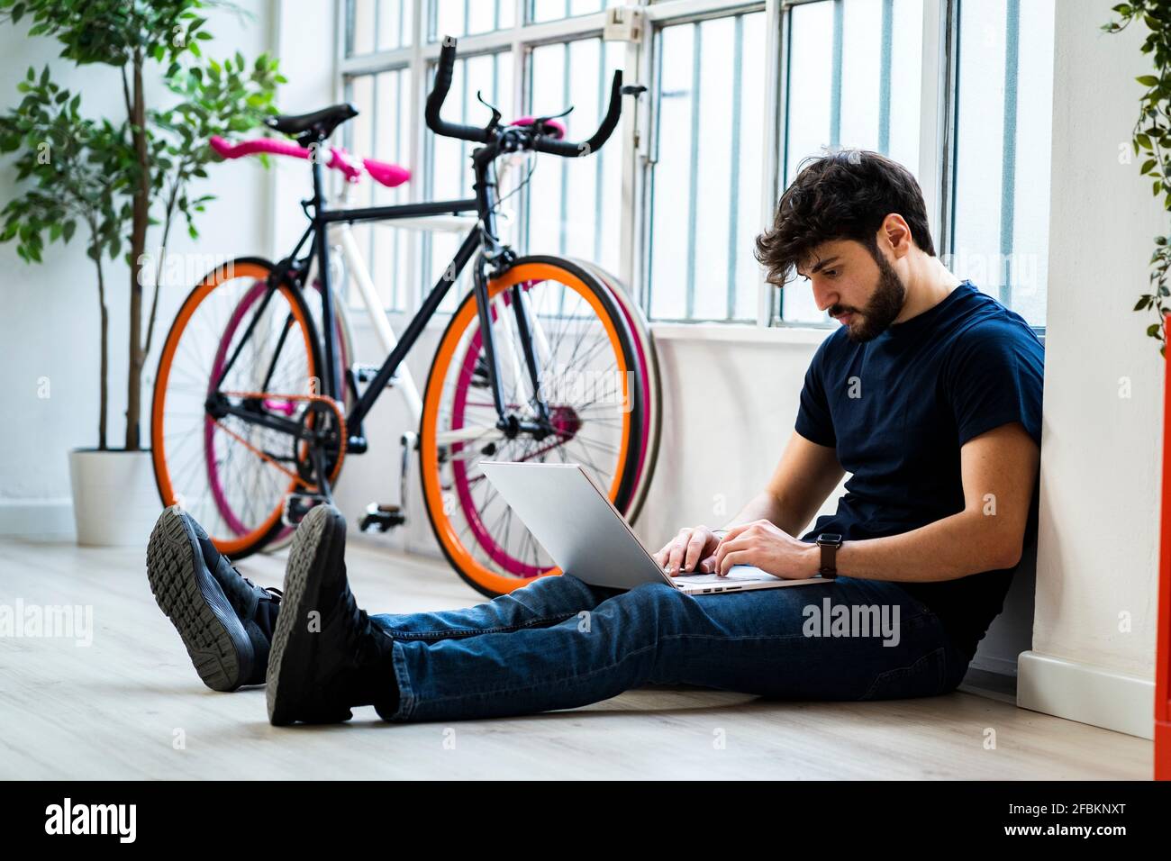 Uomo rilassato che usa il computer portatile mentre si siede vicino alle biciclette a casa Foto Stock