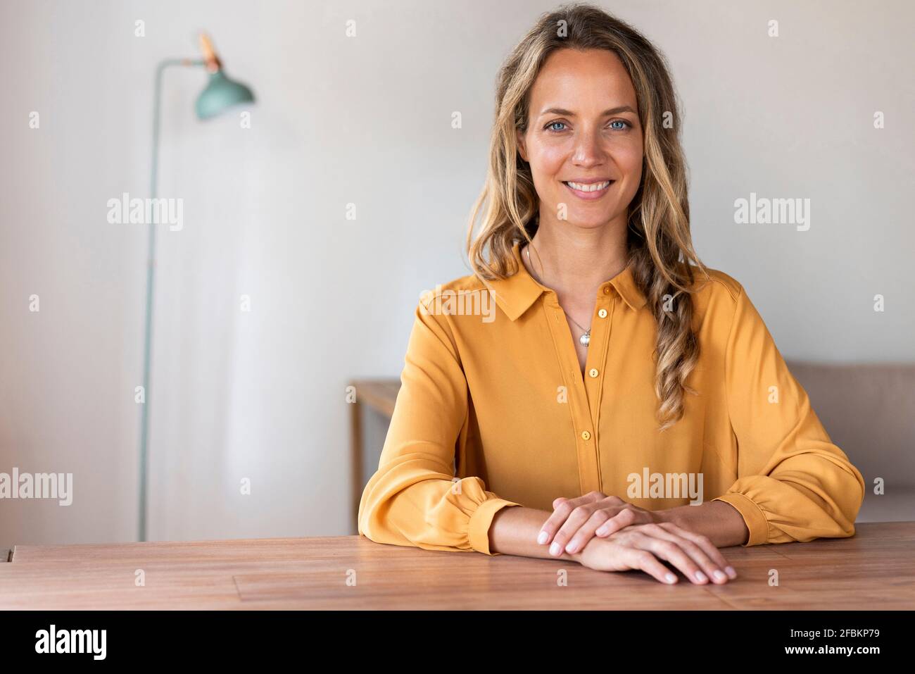 Donna sorridente con gli occhi blu seduti al tavolo Foto Stock