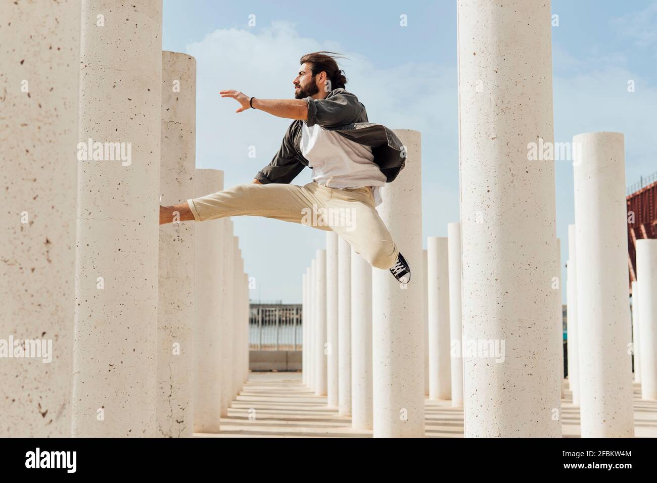 Giovane uomo spensierato che salta tra colonne bianche in giornata di sole Foto Stock