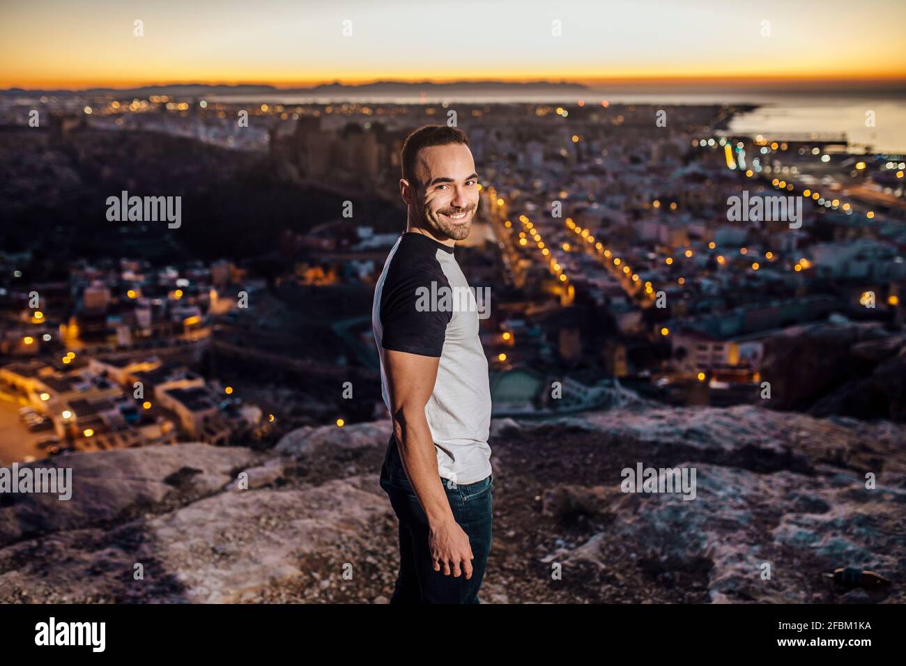 Uomo sorridente che si affaccia sulle spalle della montagna durante l'alba Foto Stock