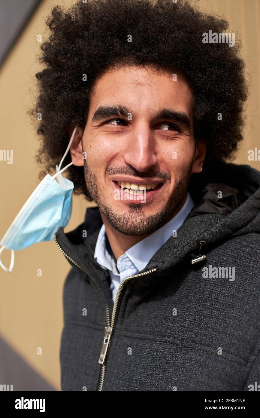 Afro uomo guardando via con maschera protettiva sul viso appeso orecchio Foto Stock