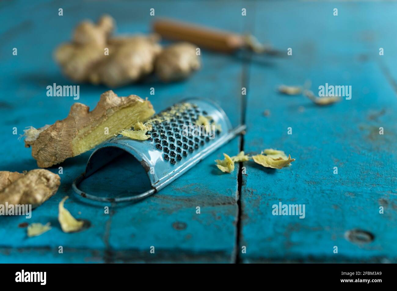 Radice di zenzero e grattugia giacenti su una superficie di legno blu Foto Stock