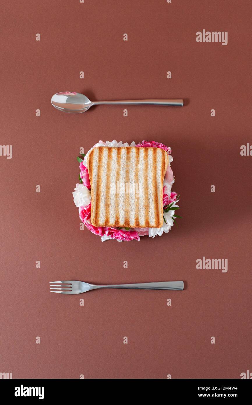Layout creativo con un sandwich e fiori luminosi su uno sfondo in terracotta color pastello. Posare piatto cibo sano minimo. Foto Stock