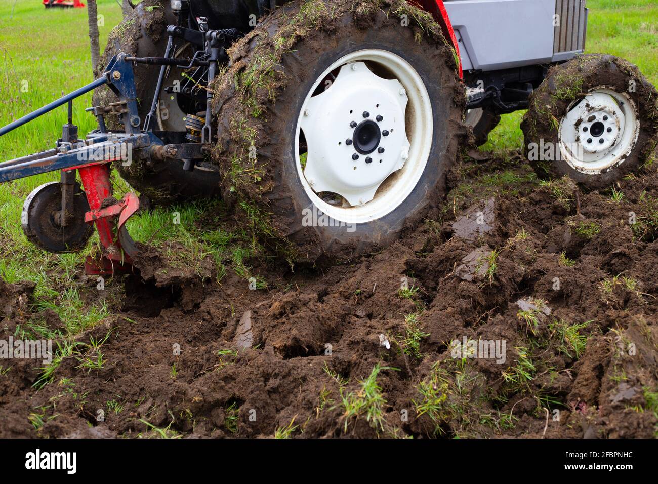 Un trattore con un aratro aratura un campo agricolo in primavera per piantare patate. Arando la terra, primo piano. Foto Stock