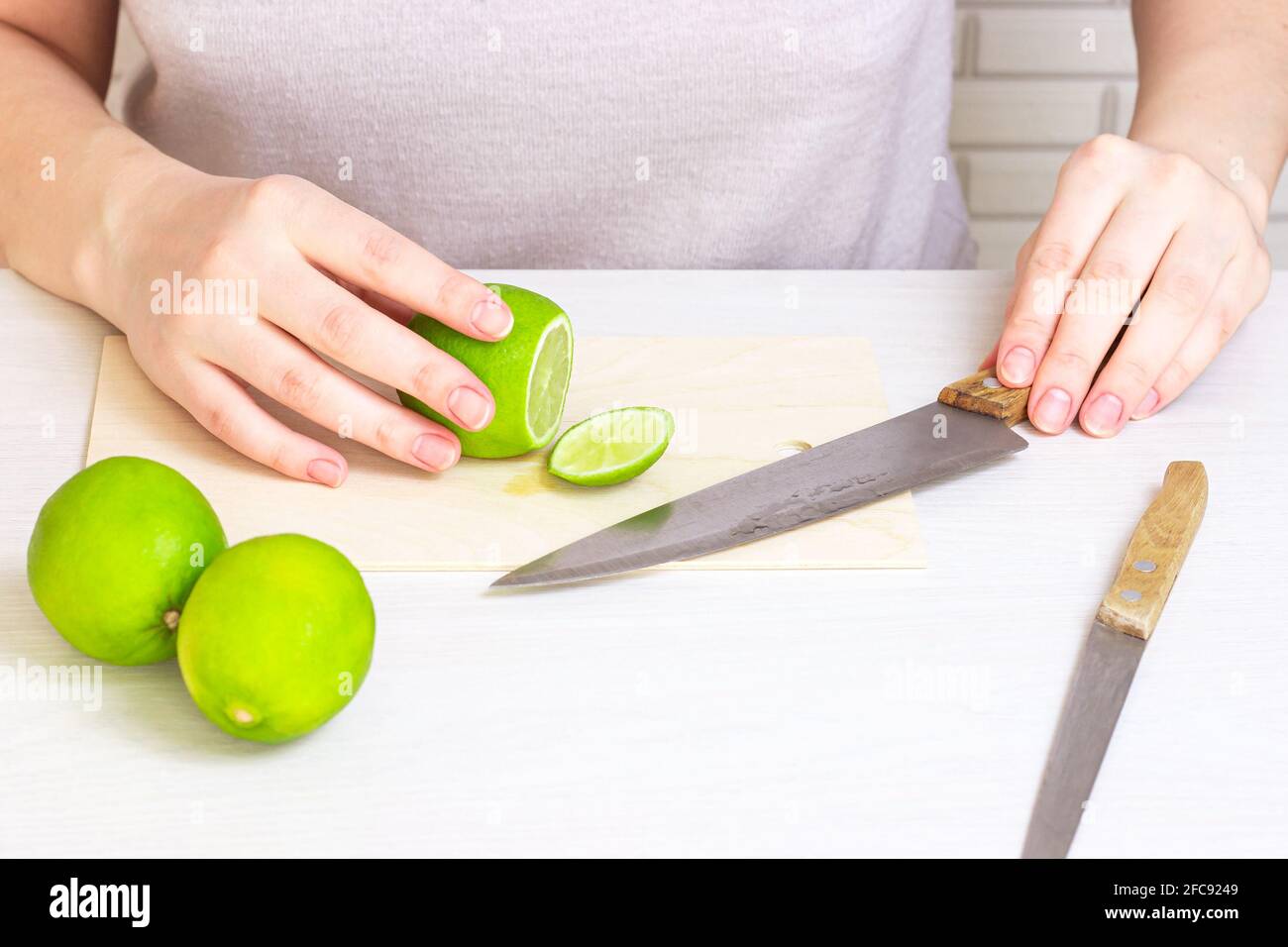 Tiglio fresco verde acido tagliato con il coltello su tagliere di legno chiaro da mani donna in cucina. Foto Stock