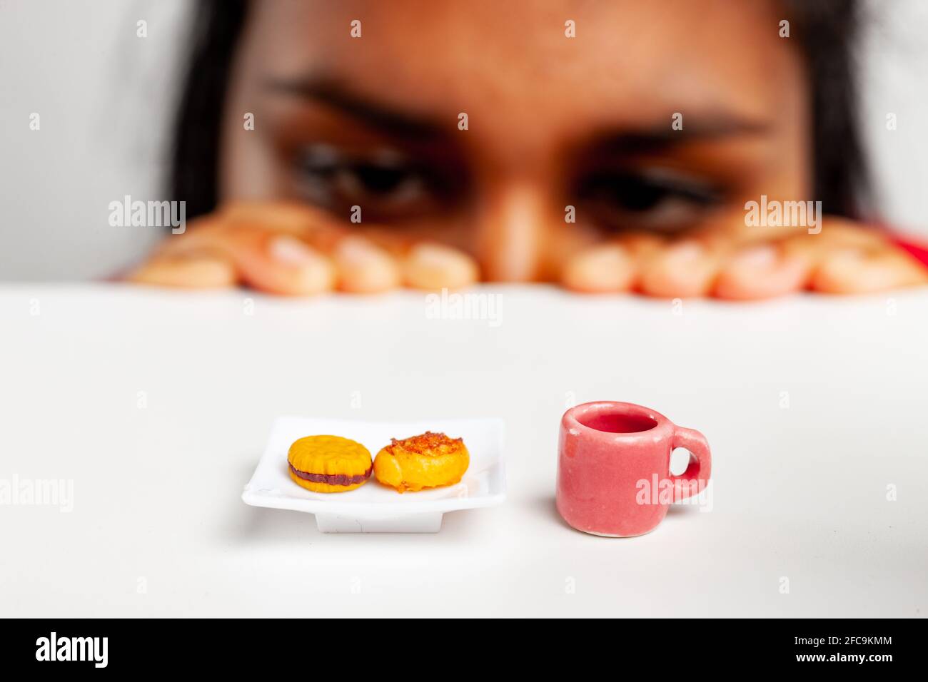 Donna che guarda a lungo ad un piatto invitante di pasticceria e. tazza di caffè in un'immagine di cibo divertente utilizzando la miniatura rinfreschi con focus selettivo Foto Stock