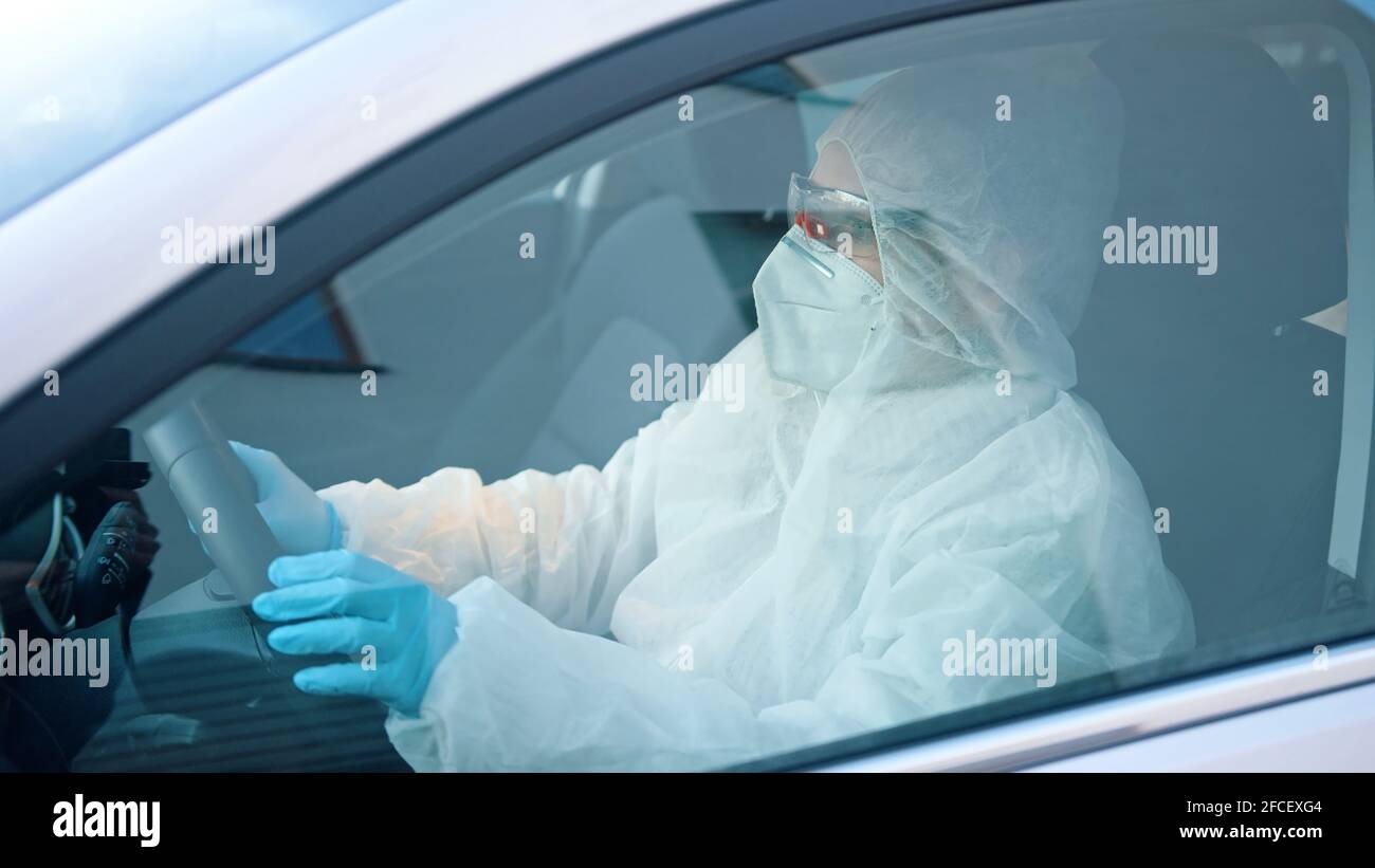 Persona non identificabile in tuta protettiva auto guida. Vista del finestrino laterale della vettura su uomo nell'area a rischio di infezione. Foto di alta qualità Foto Stock