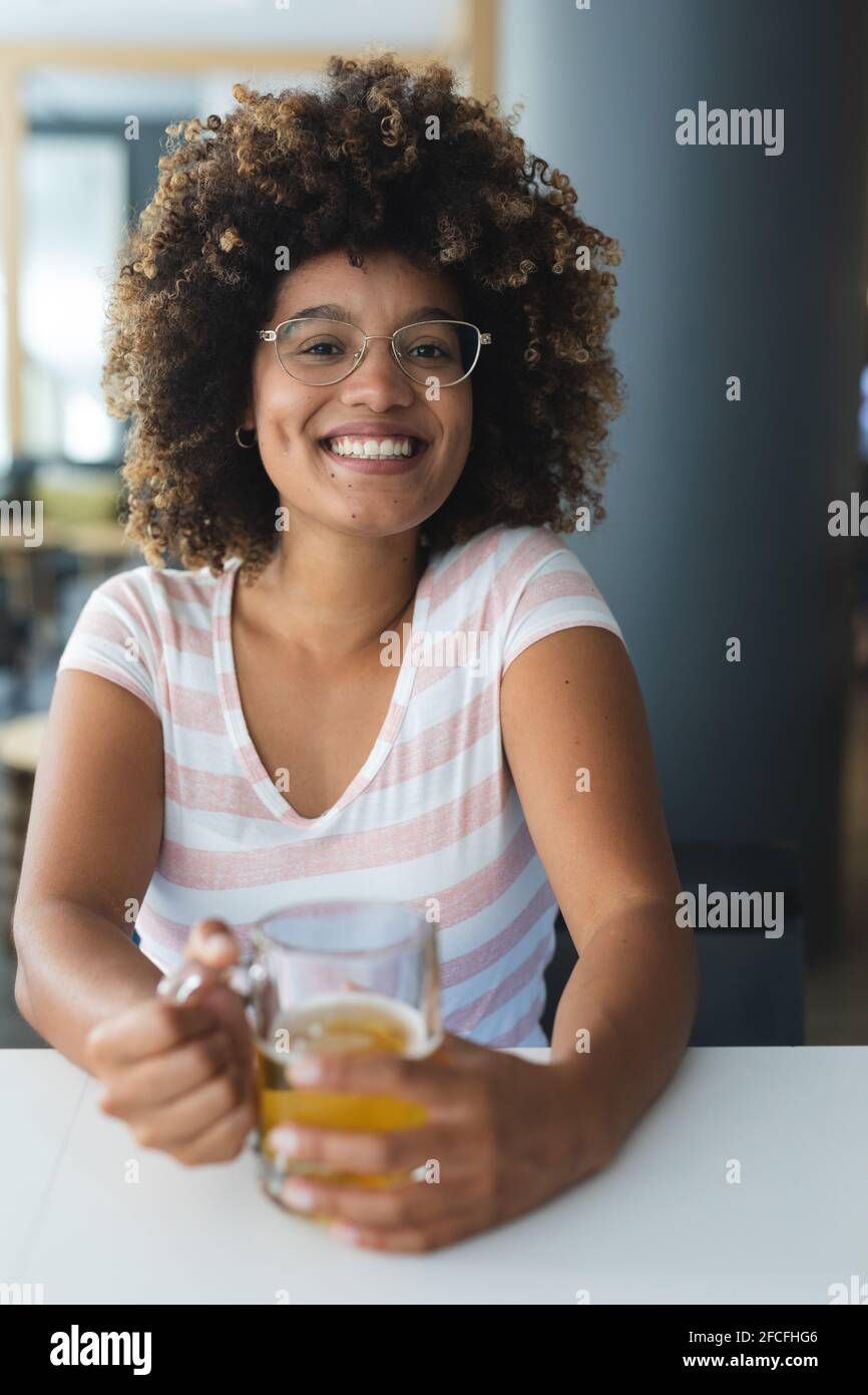 Ritratto di razza mista donna seduta al tavolo sorridente avere birra Foto Stock