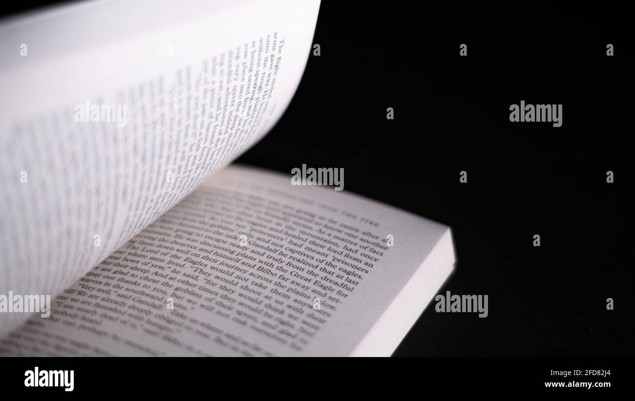 Pagine di scorrimento in un libro di romanzo inglese. Libro aperto isolato in uno sfondo nero scuro. Concetto di lettura fa un uomo pieno. Foto Stock