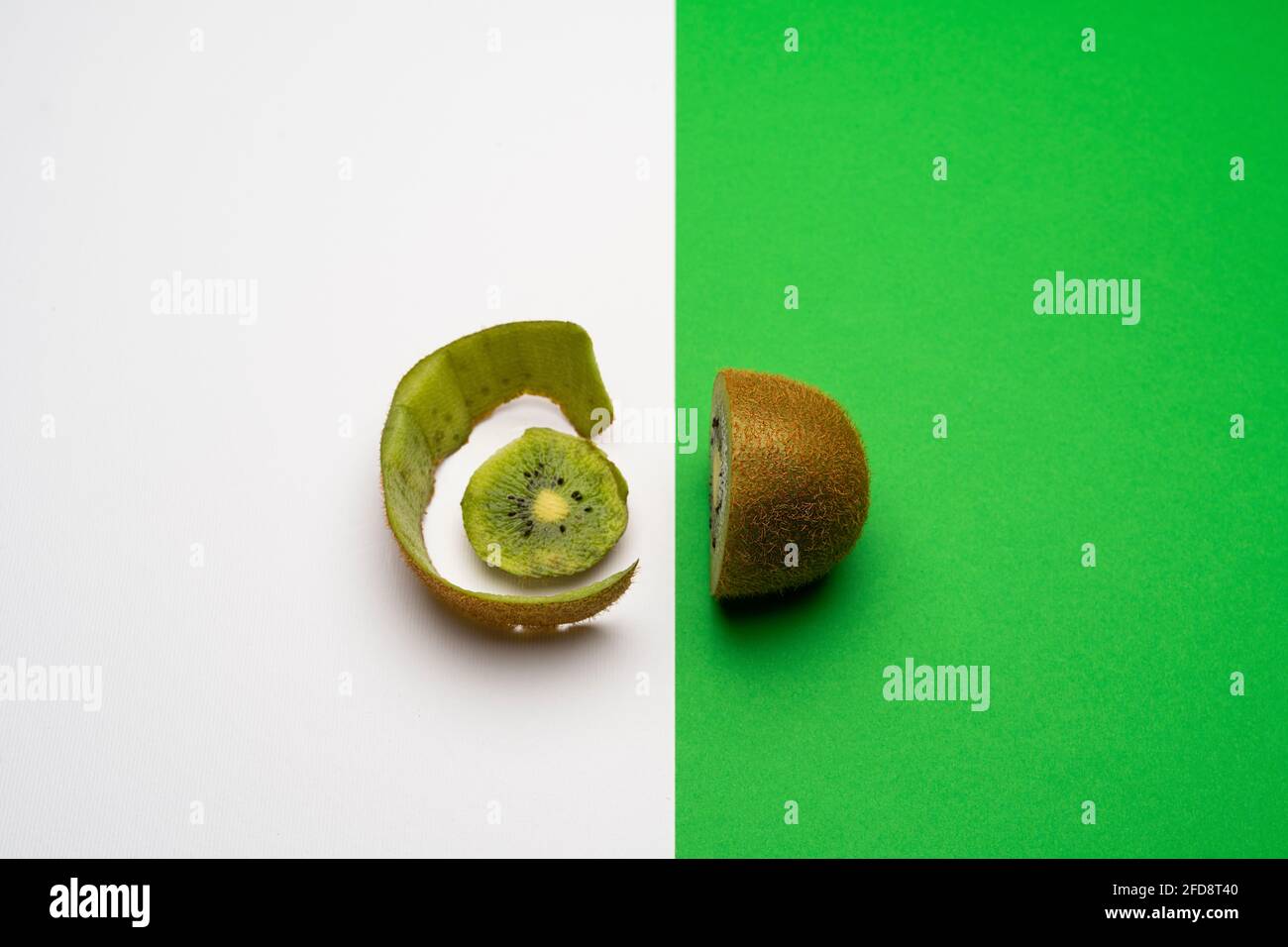 un kiwi tagliato, metà sulla superficie verde e la buccia su una superficie bianca Foto Stock