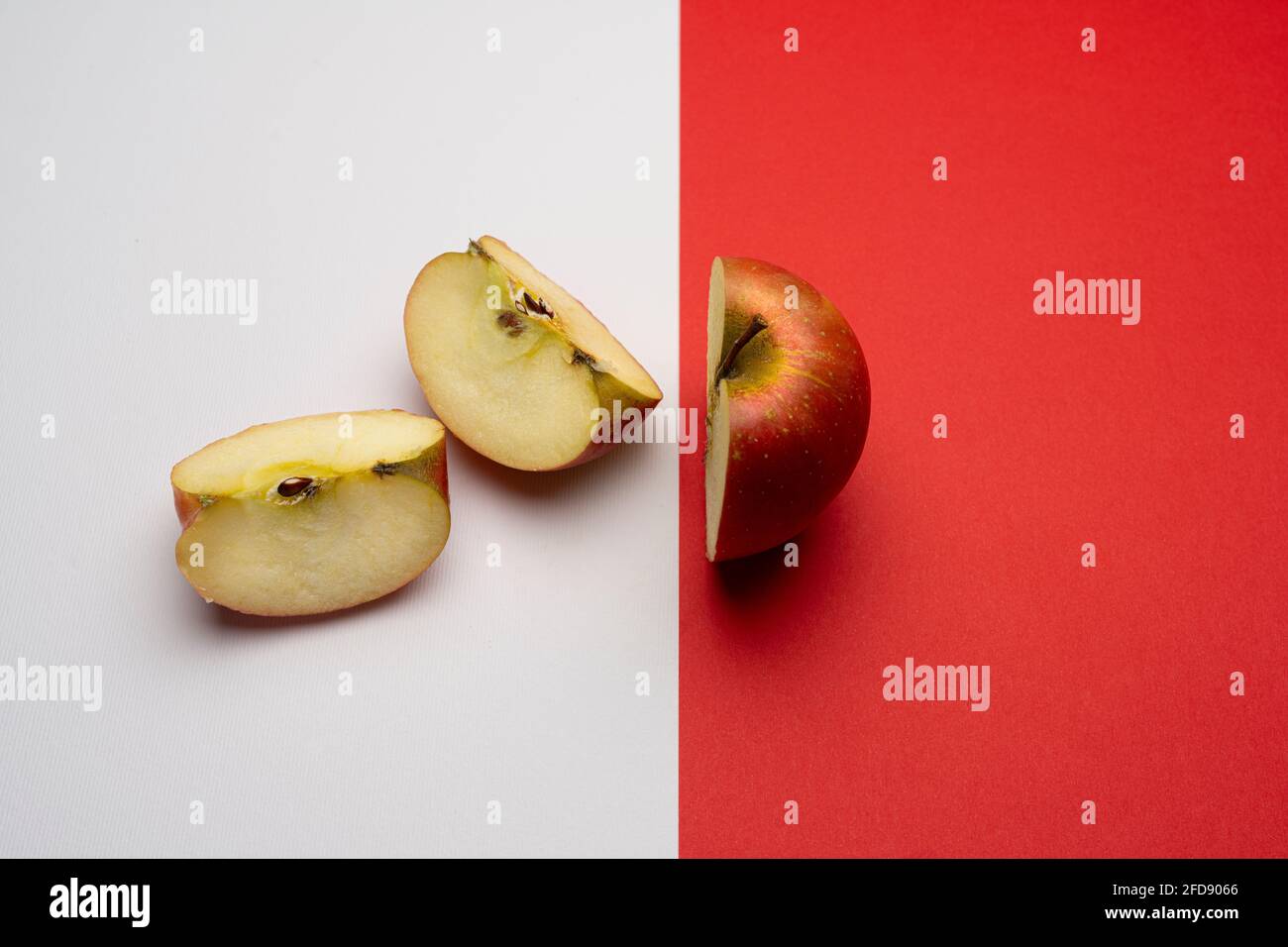 una mela tagliata, metà sulla superficie rossa e l'altra metà tagliata su una superficie bianca Foto Stock