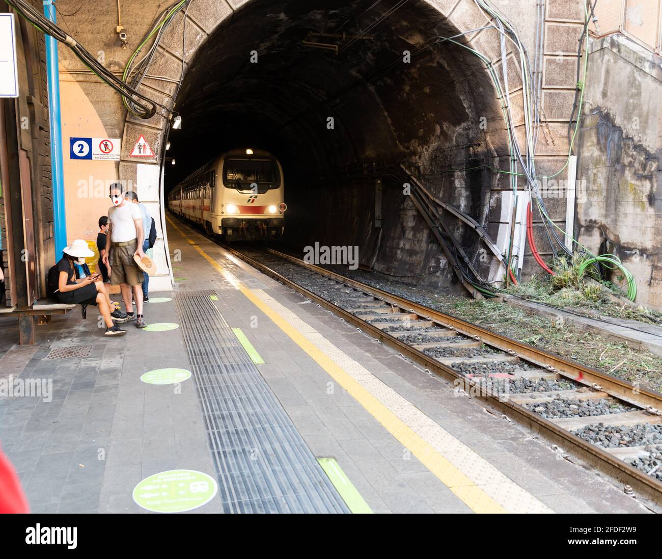 Vernazza, Liguria, Italia. Giugno 2021. La stazione ferroviaria è adiacente all'uscita del tunnel. Il treno sta arrivando, i viaggiatori stanno aspettando sul piatto Foto Stock