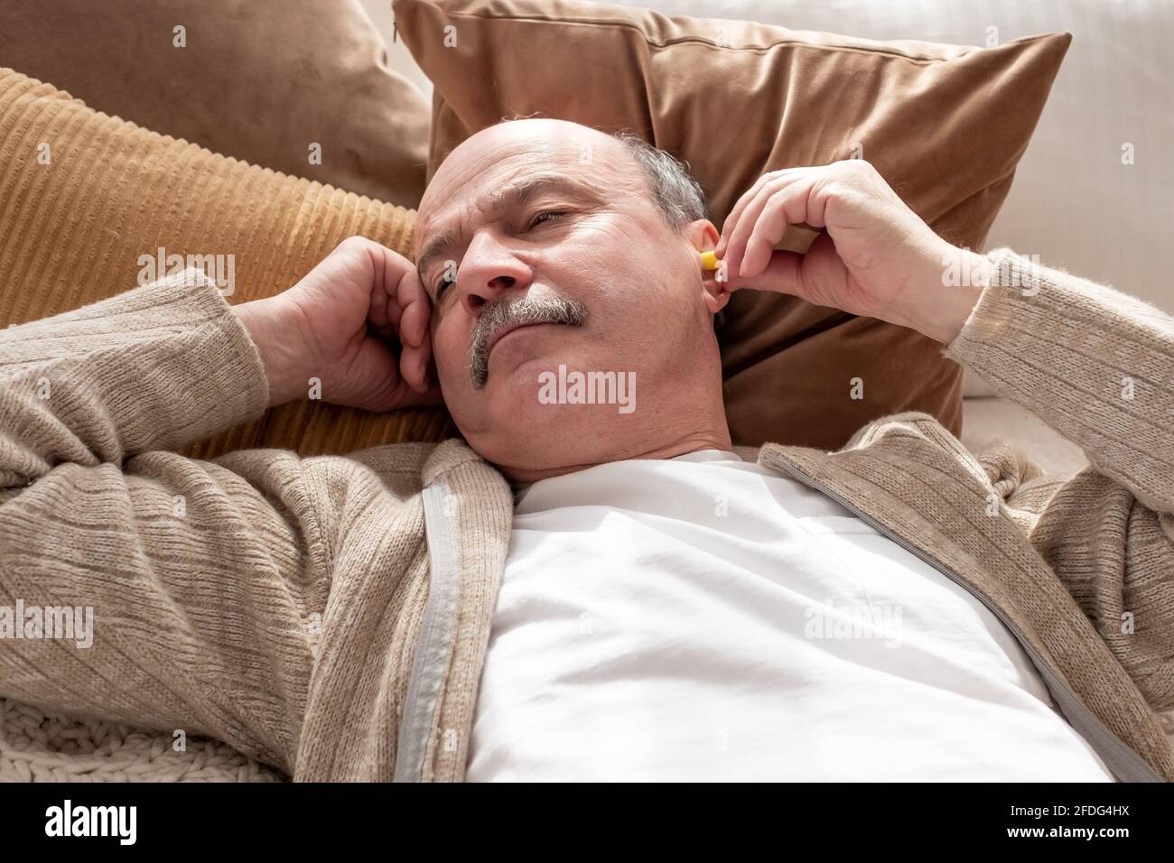 L'anziano caucasico ha sollecitato l'uomo che tiene un tappo giallo dell'orecchio che prova a. sonno con insonnia che riposa a casa da sola Foto Stock