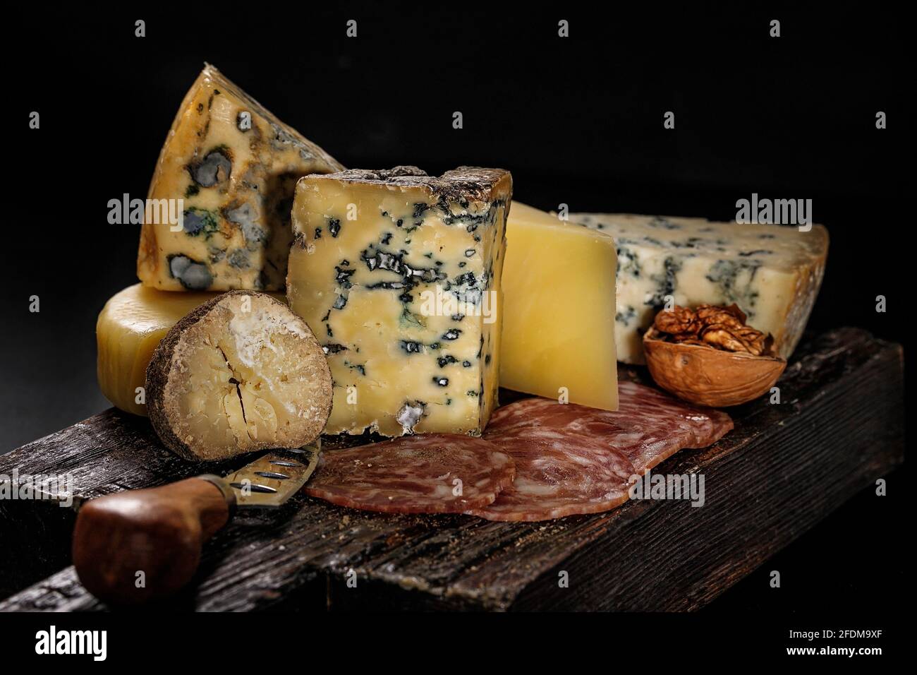 Vari formaggi gourmet assortiti e salsicce affumicate crude su una tavola di legno su sfondo scuro. Vari tipi di formaggio: Duro e morbido con muffa. Escl Foto Stock